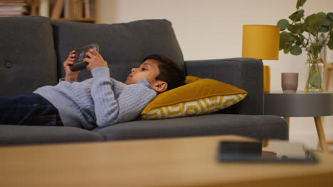 Young-Boy-Lying-On-Sofa-At-Home-Playing-Game-Or-Streaming-Onto-Handheld-Gaming-Device-7